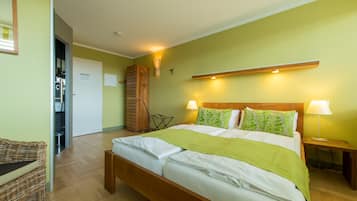 Una cama bien tendida con cabecera de madera, dos lámparas de noche y una manta verde.