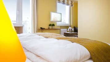 Ein Hotelzimmer mit Bett, einem Fenster mit Vorhängen, einem kleinen Tisch mit Telefon und Pflanze sowie einem Heizkörper.