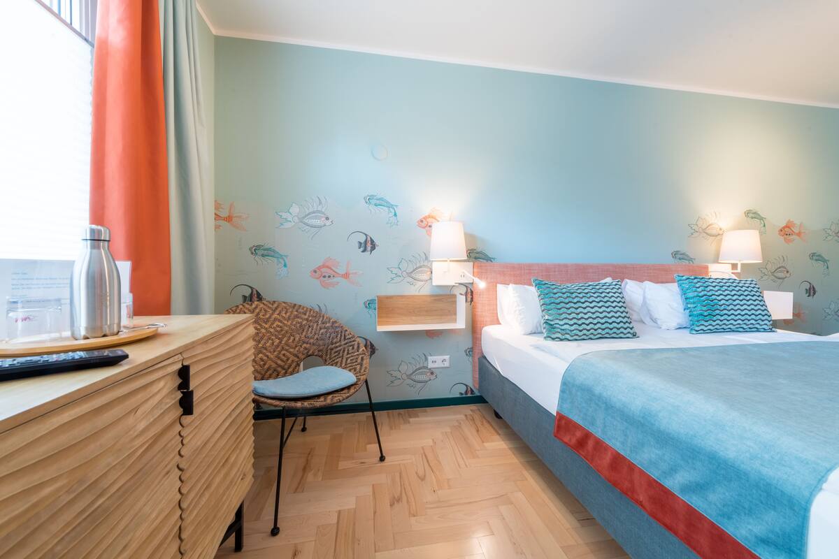A hotel room with a bed, a desk, a chair, and a wall with fish decals.