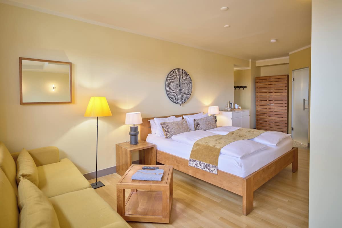 A bedroom with a bed, bedside tables, a lamp, a mirror, a wall decoration, a wardrobe, and a sofa.