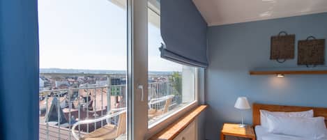 Une chambre avec une grande fenêtre, un lit, une table de chevet et une vue sur la ville.