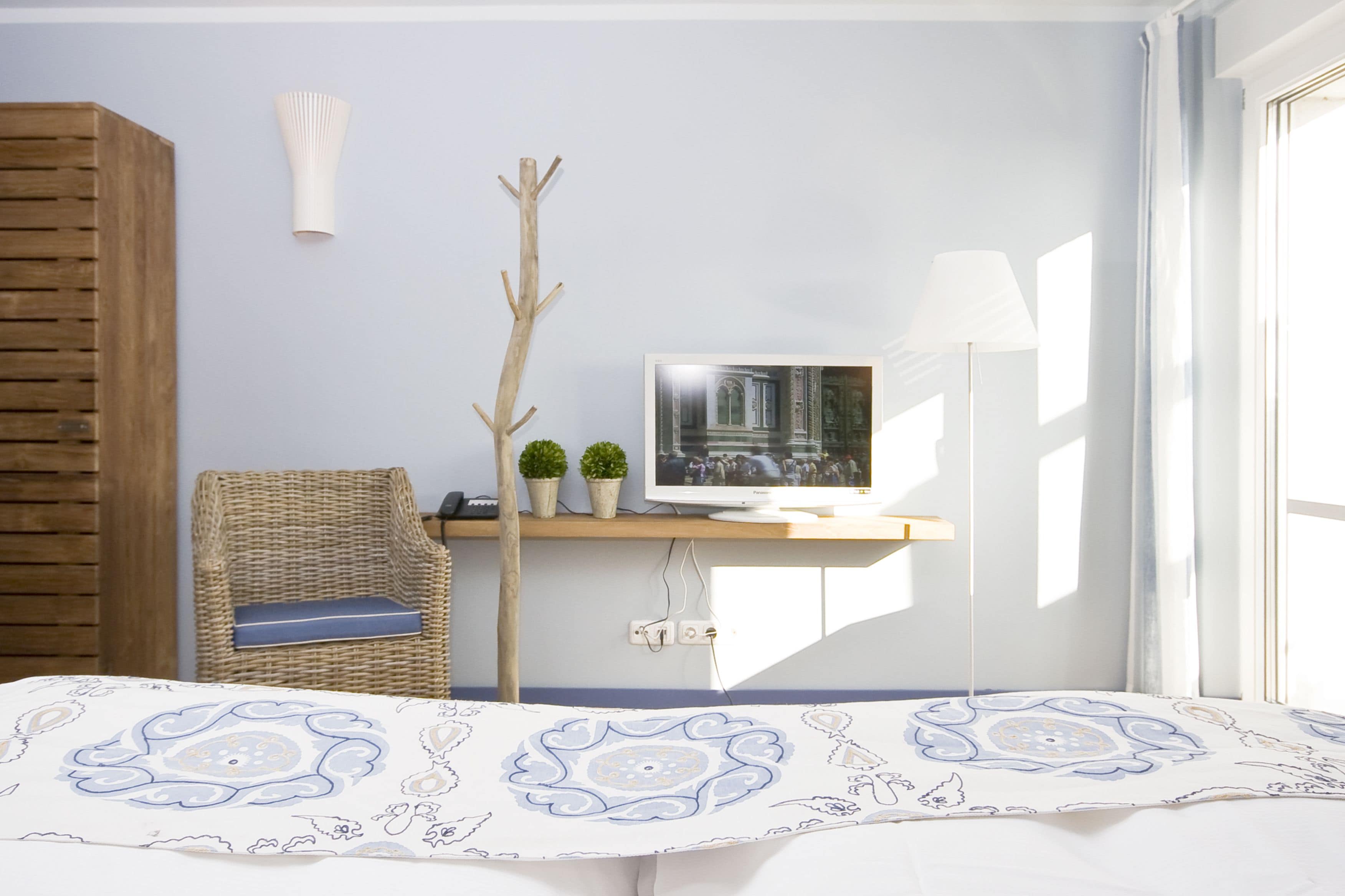 Ein Schlafzimmer mit einem Bett, einem Fernseher auf einem Schrank, einem Korbstuhl und einem Fenster mit Vorhängen.