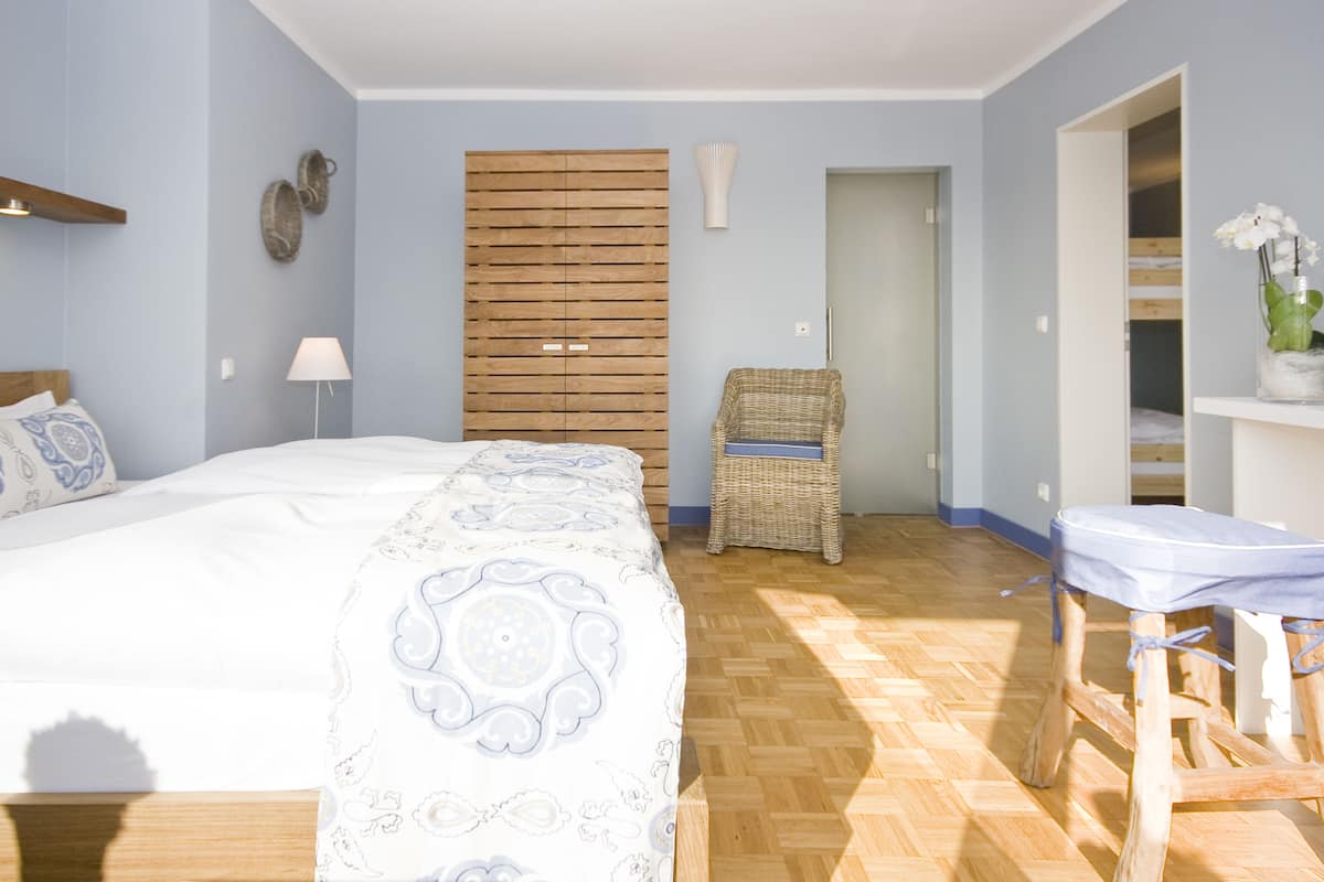 A bedroom with a bed, a wicker chair, a small table, and a wooden wardrobe.