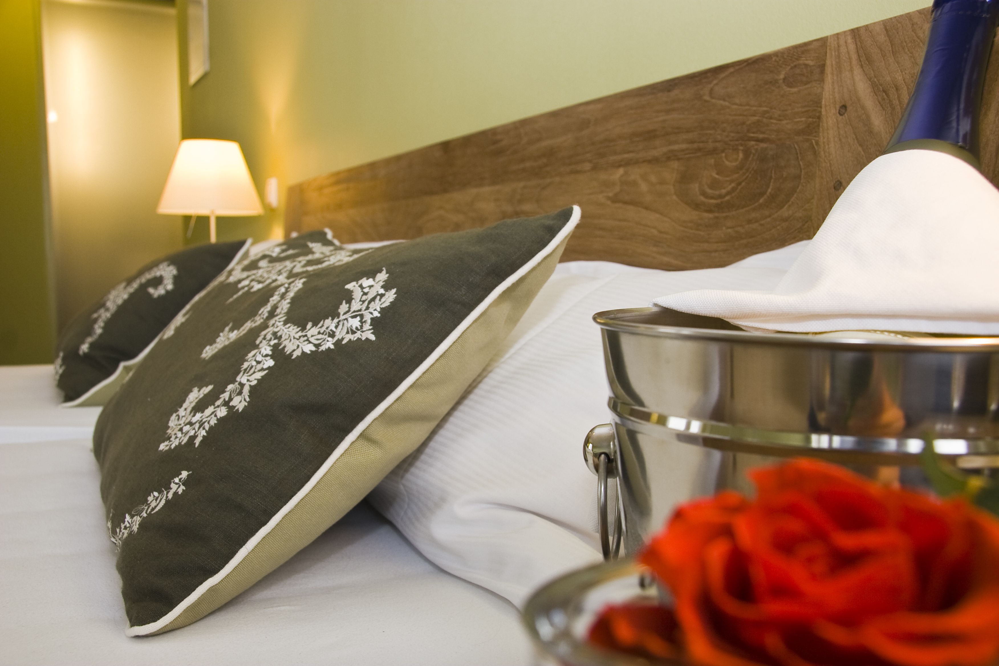 A neatly made bed with decorative pillows, a metal container, and a red rose.