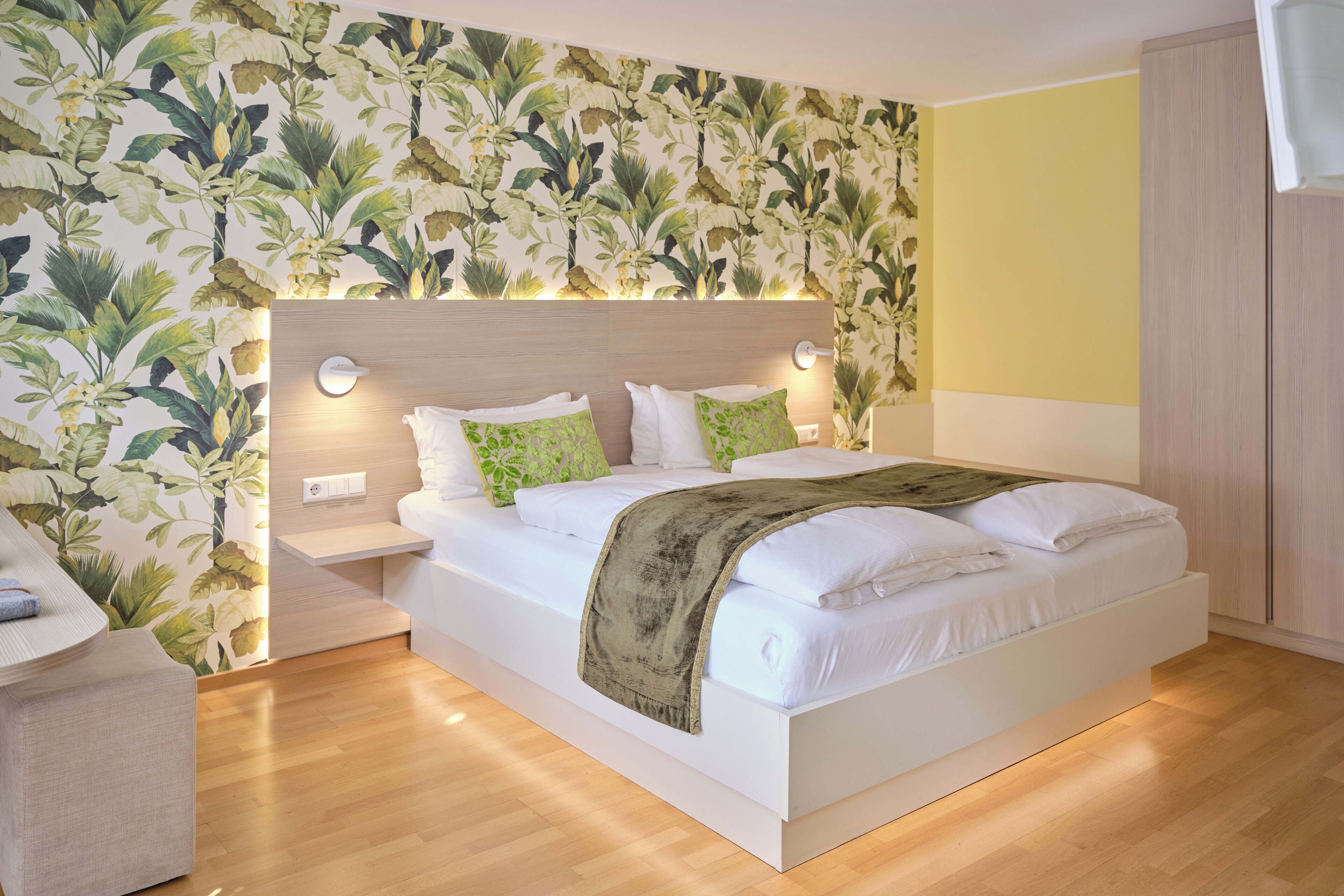 A bedroom with a bed, nightstands, a wall with a floral pattern, and a yellow accent wall.
