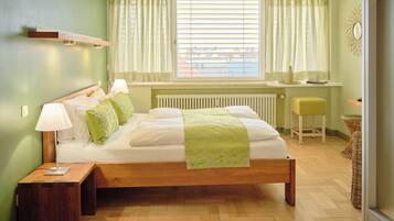 Un dormitorio con cama de madera, lámparas de noche, una ventana con cortinas, un radiador y un taburete pequeño.