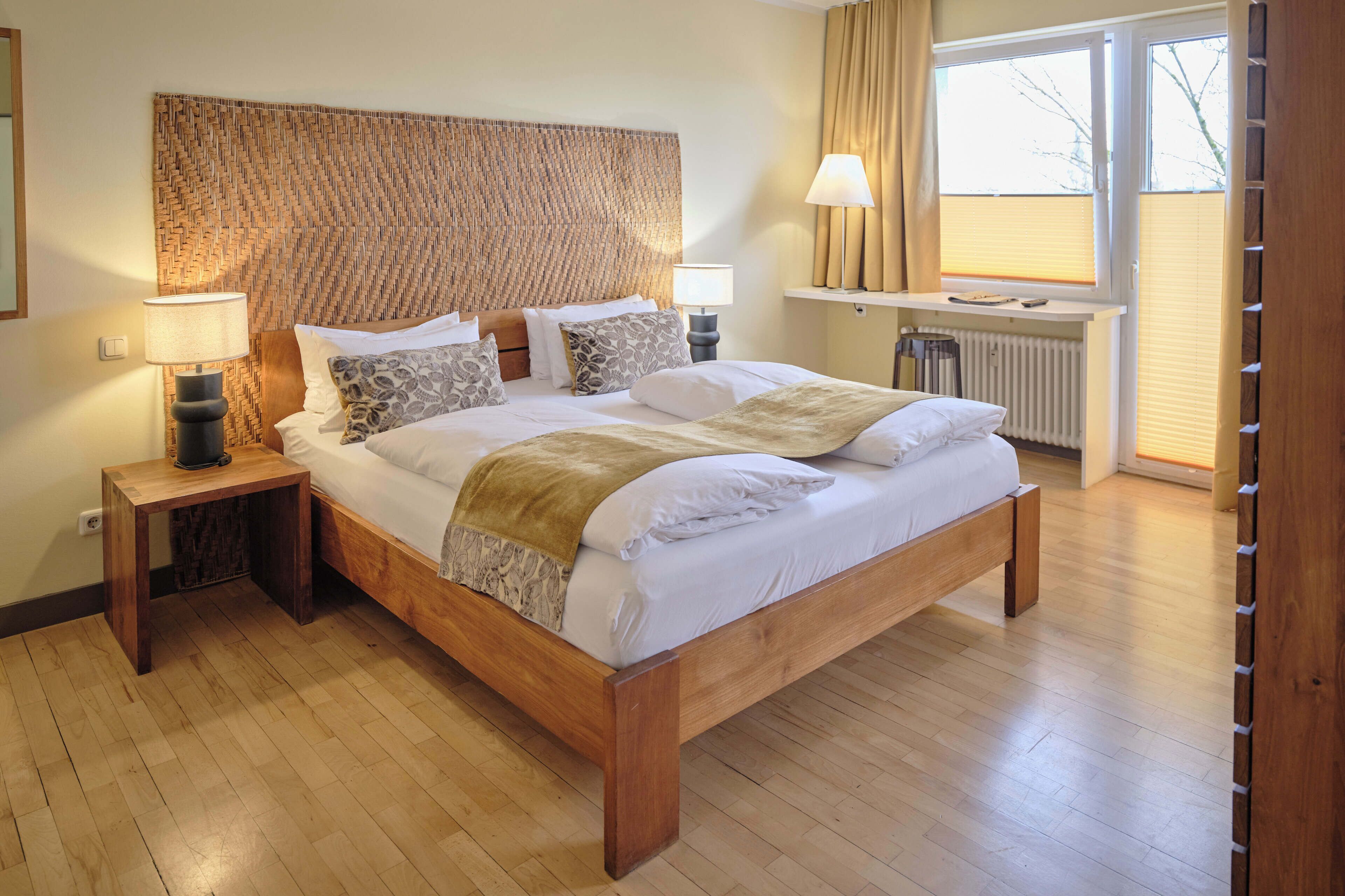 A wooden bed with a woven headboard, bedside lamps, and a window with curtains.