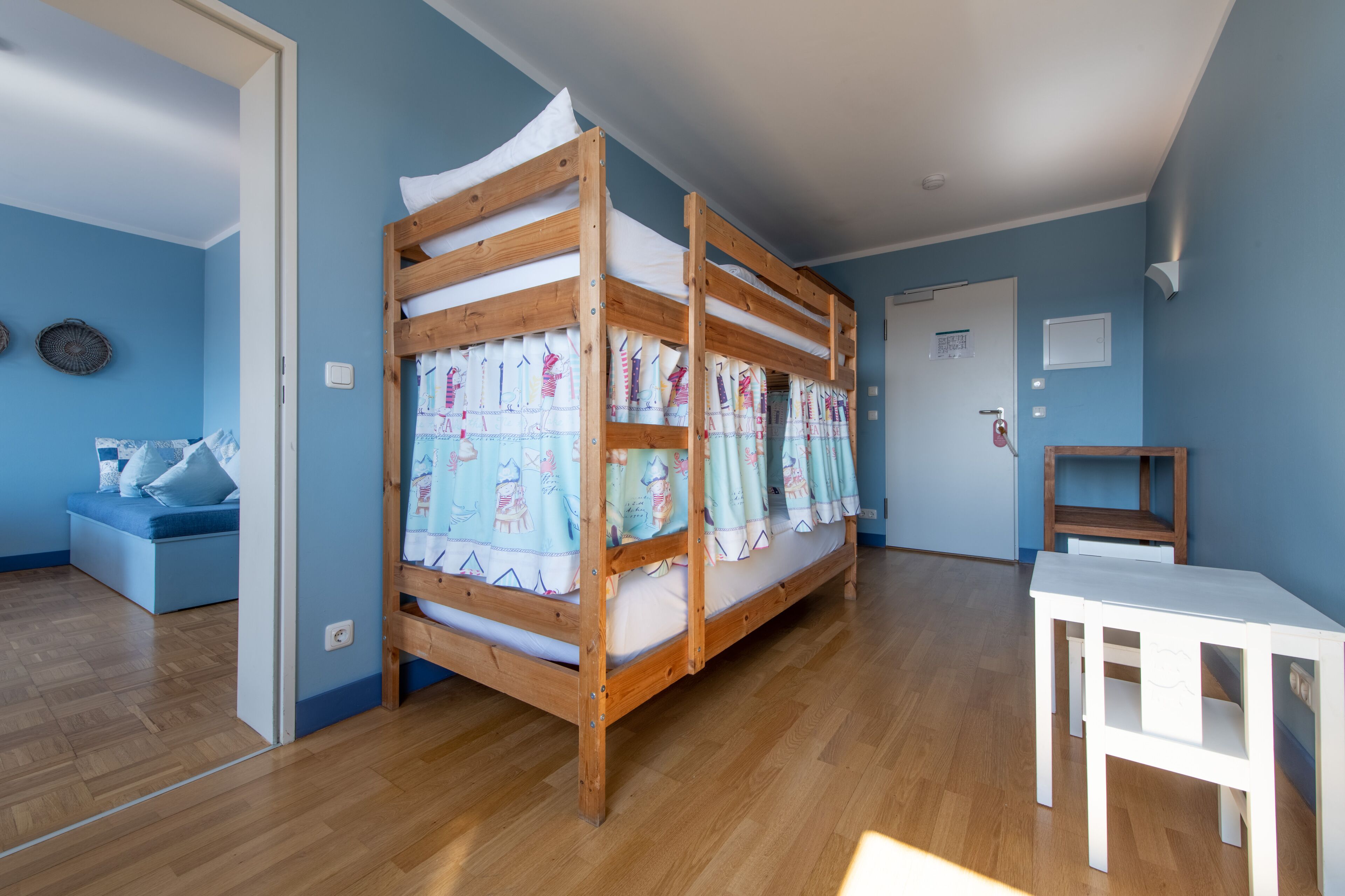 Una habitación con una cama individual doble, una mesita blanca y una pared azul.