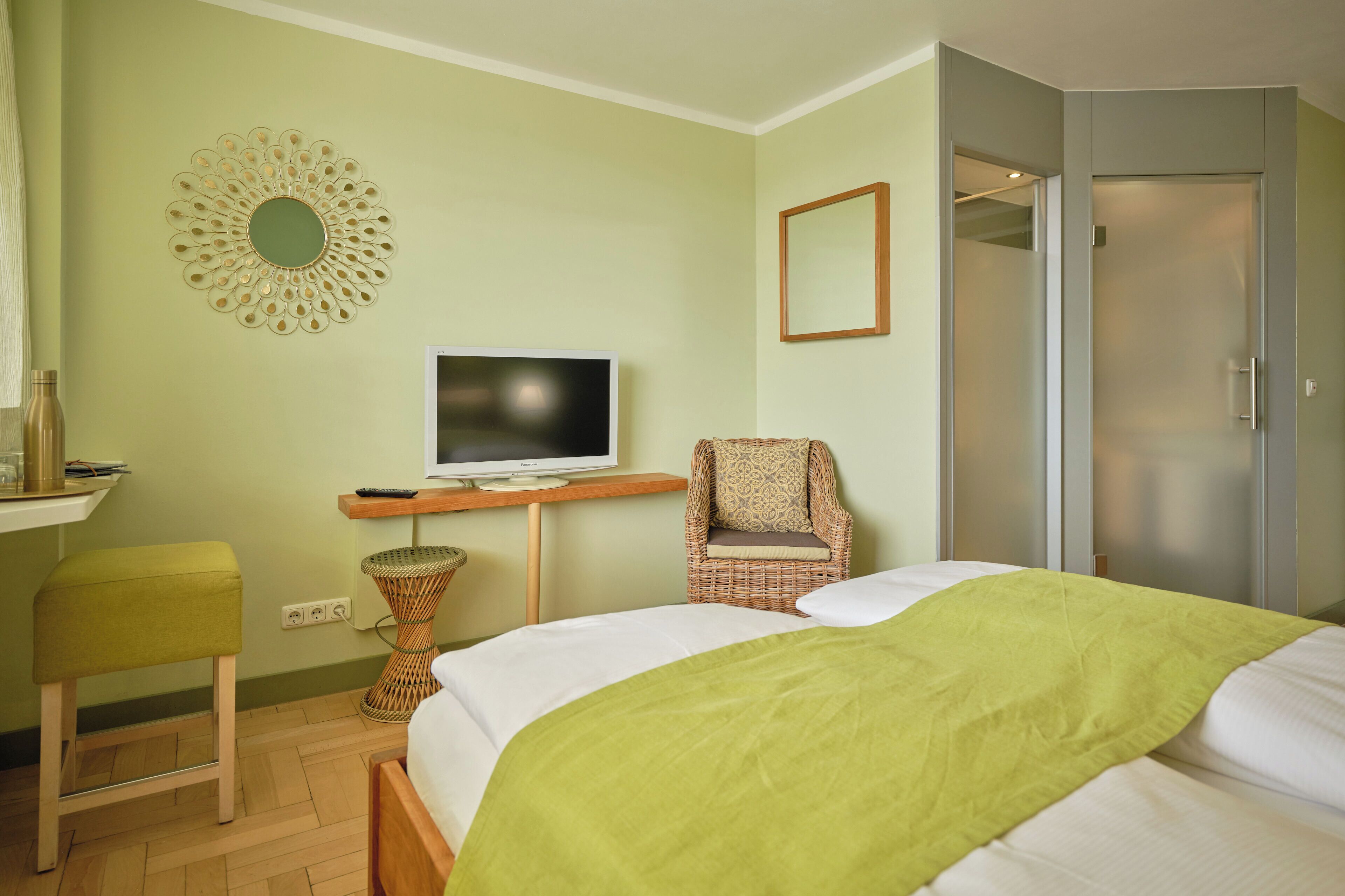 A bedroom with a bed, a television, a wicker chair, a mirror, and a wardrobe.