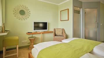 A bedroom with a bed, a television, a wicker chair, a mirror, and a wardrobe.