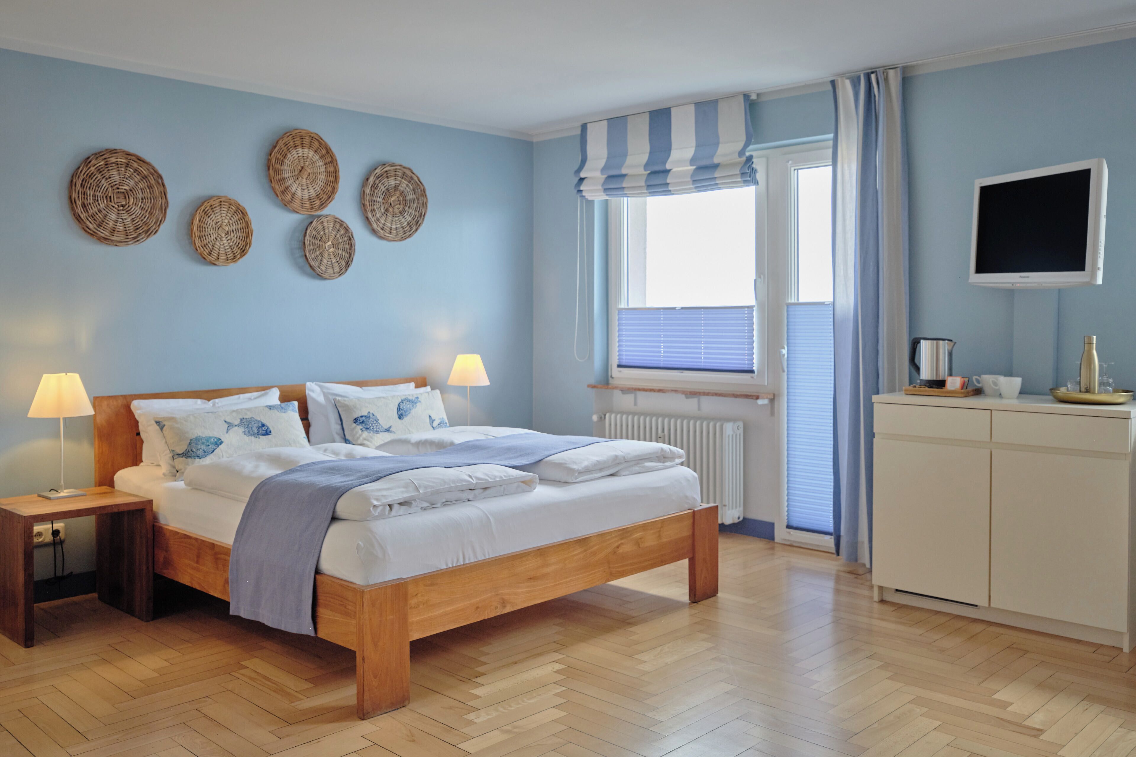 Quarto com cama de madeira, luminárias de cabeceira, televisão e janela com cortinas.