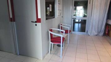 A hallway with a door, two chairs with red cushions, and a tiled floor.