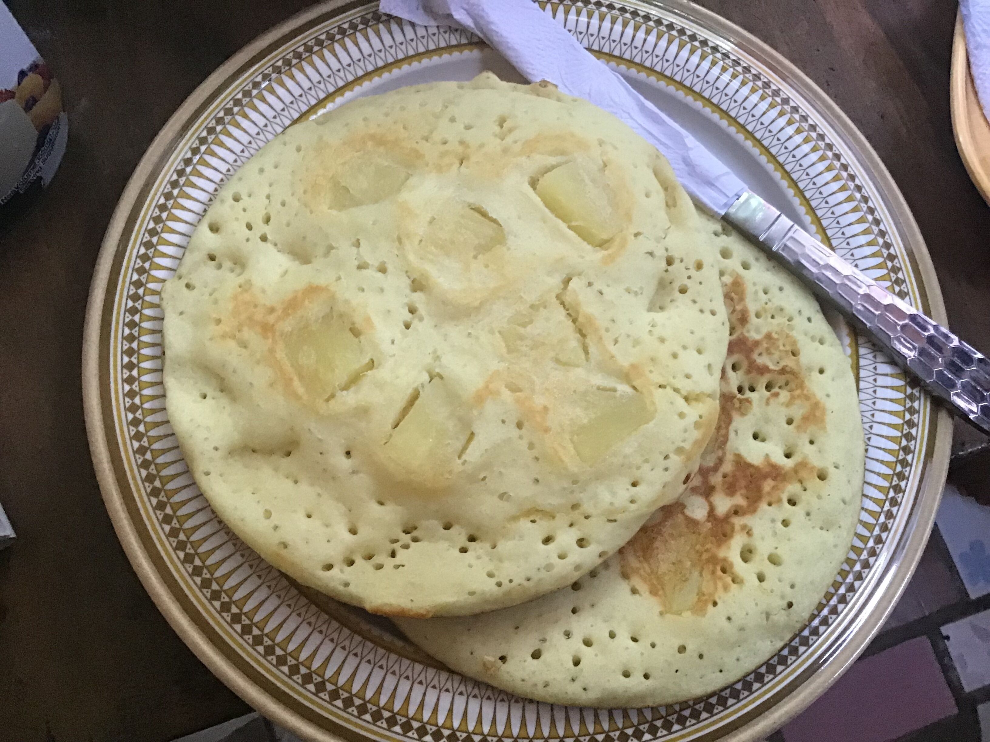 A plate with two round, hole-ridden flatbreads, one with a piece of butter, on a patterned plate.