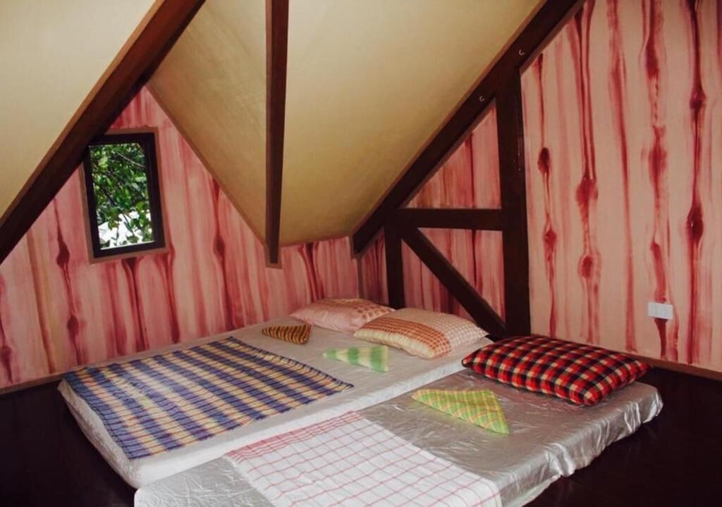 A bedroom with a sloped ceiling, a window, and a bed with multiple pillows and a blanket.