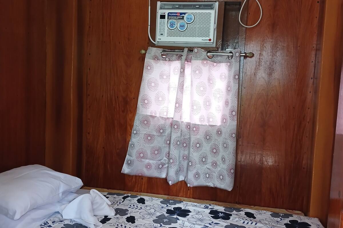 A small, compact room with a bed, a wall-mounted air conditioner, and a curtain.