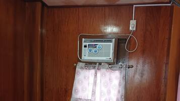 Una habitación pequeña y funcional con cama, aire acondicionado de pared y cortina.
