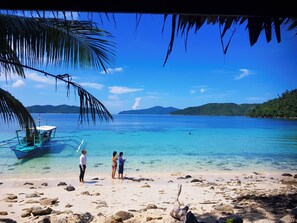 A beach with clear turquoise water, a boat, and rocky shore. - Ferranco Tourist Inn (San Vicente)