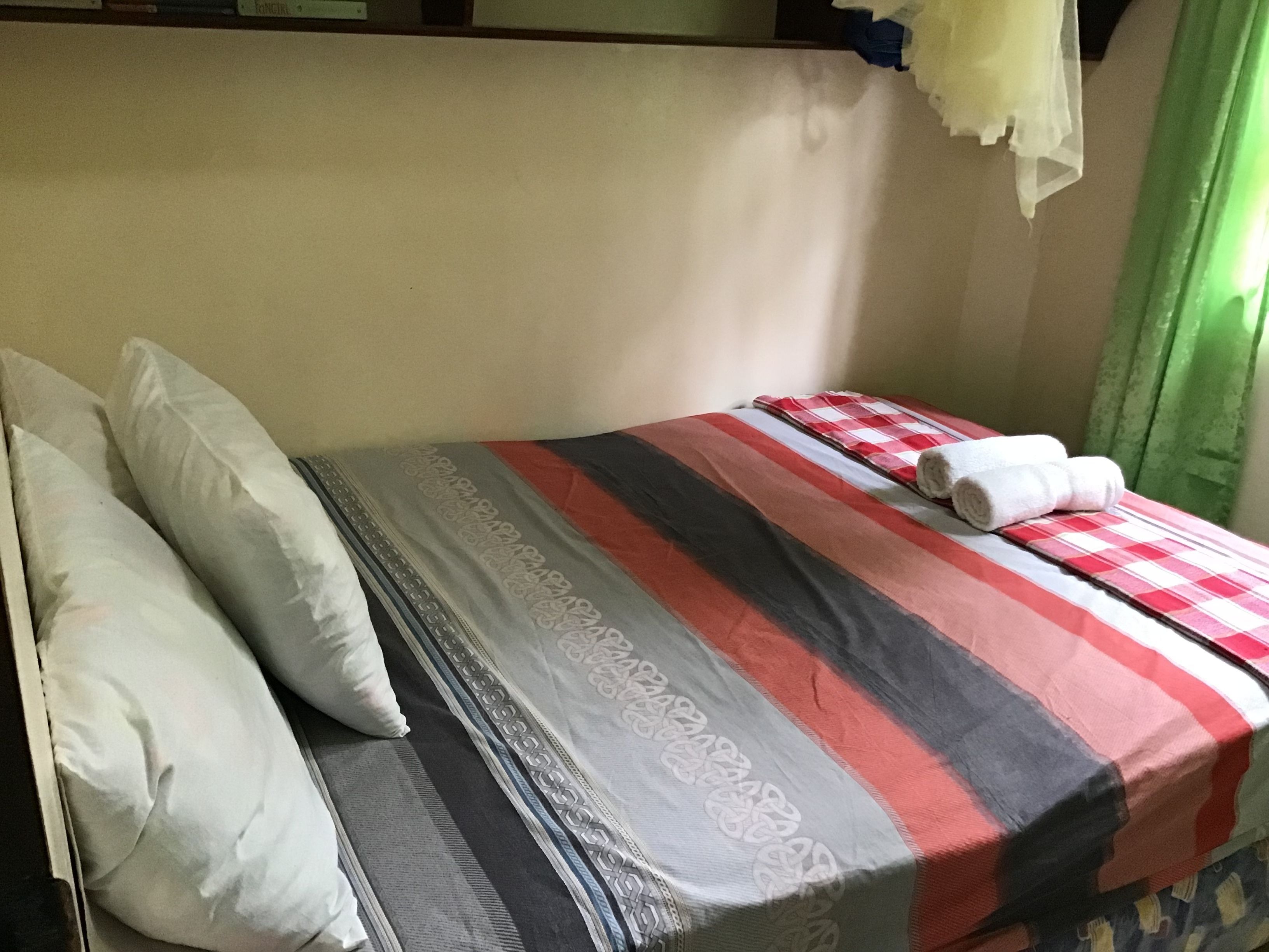 Uma cama de solteiro com um edredom listrado, duas almofadas e duas toalhas enroladas.