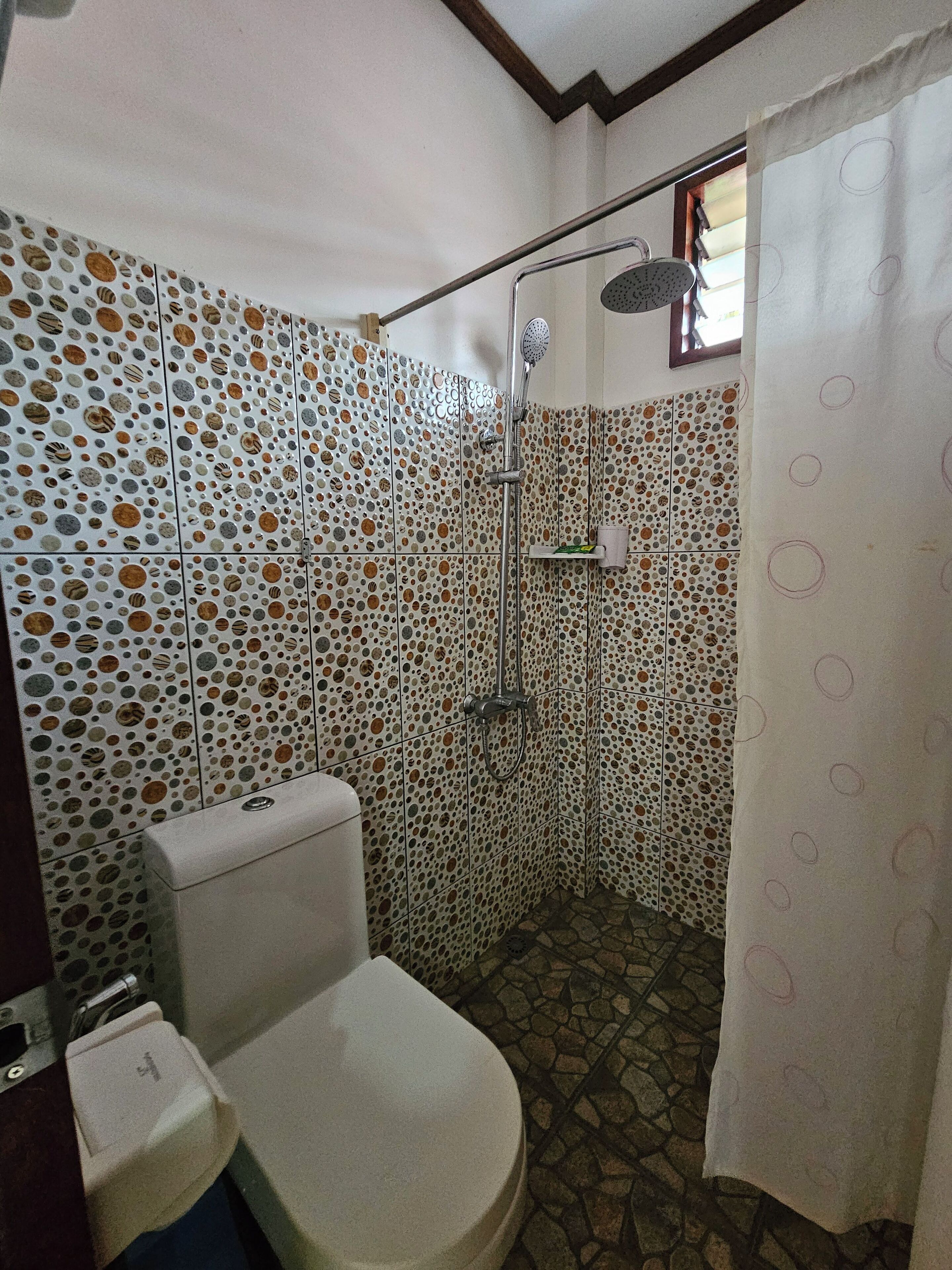 Un baño con inodoro, ducha y baldosas estampadas.
