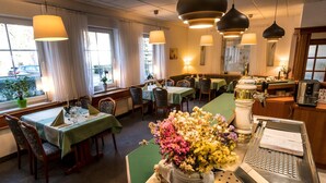 A restaurant with multiple tables and chairs, a coffee machine, and a vase of flowers on the counter. - Pension & Restaurant Nordstern (Cottbus)