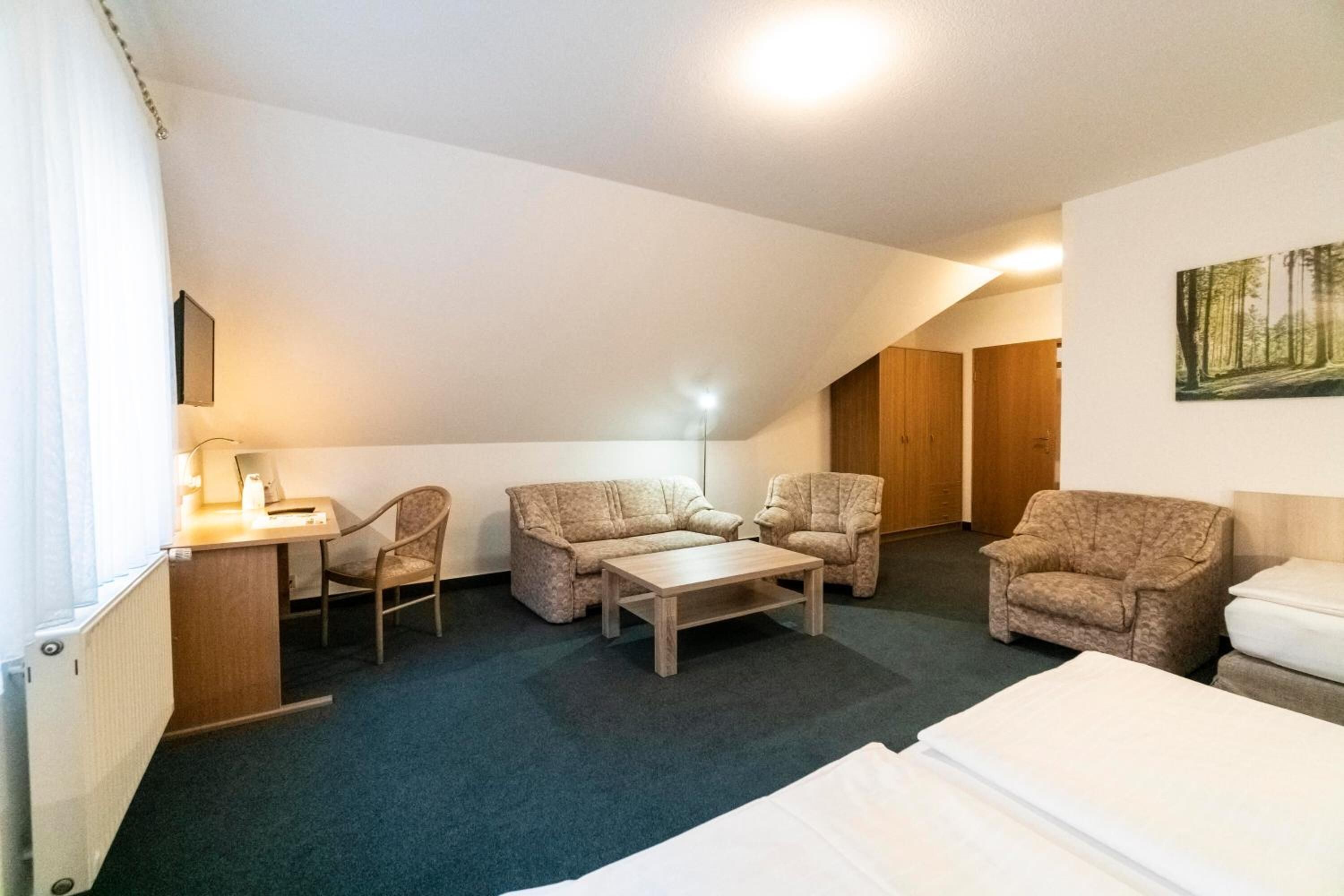 A hotel room with a desk, two armchairs, a sofa, a coffee table, and a bed.