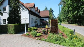A residential building with a tiled roof, a paved driveway, and a garden area with a bench and potted plants. - Pension & Restaurant Nordstern (Cottbus)