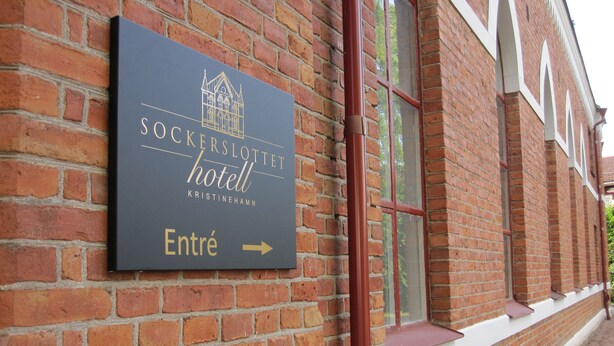A brick building with a sign for the "Sockerlottet Hotel" indicating the entrance direction. - Sockerslottet hotell (Kristinehamn)