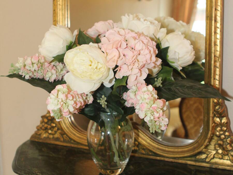 A mirror with a gold frame, a vase with flowers, and a marble table.