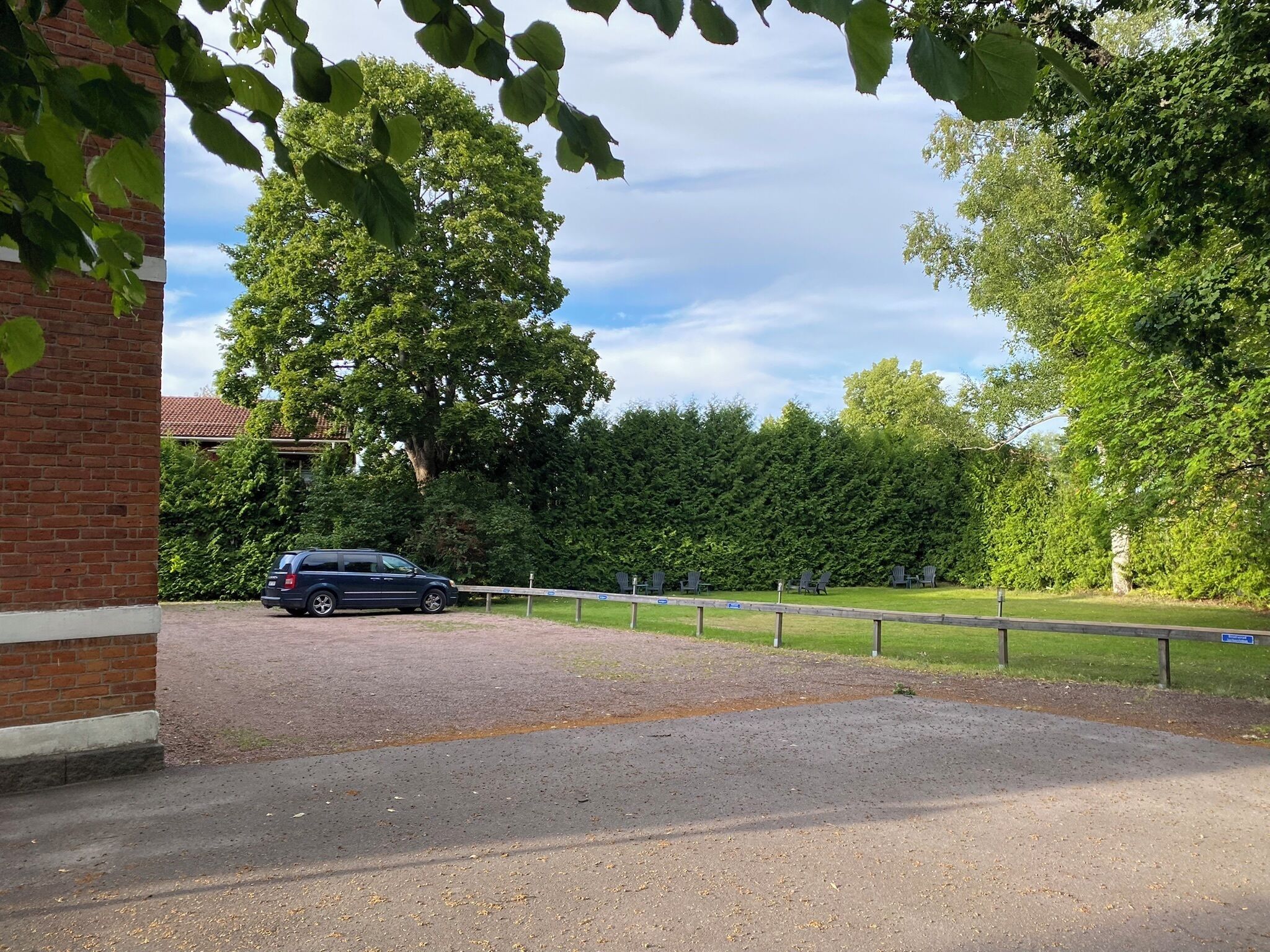 Uma área de estacionamento com piso de cascalho, um edifício de tijolos e uma fileira de cadeiras verdes.