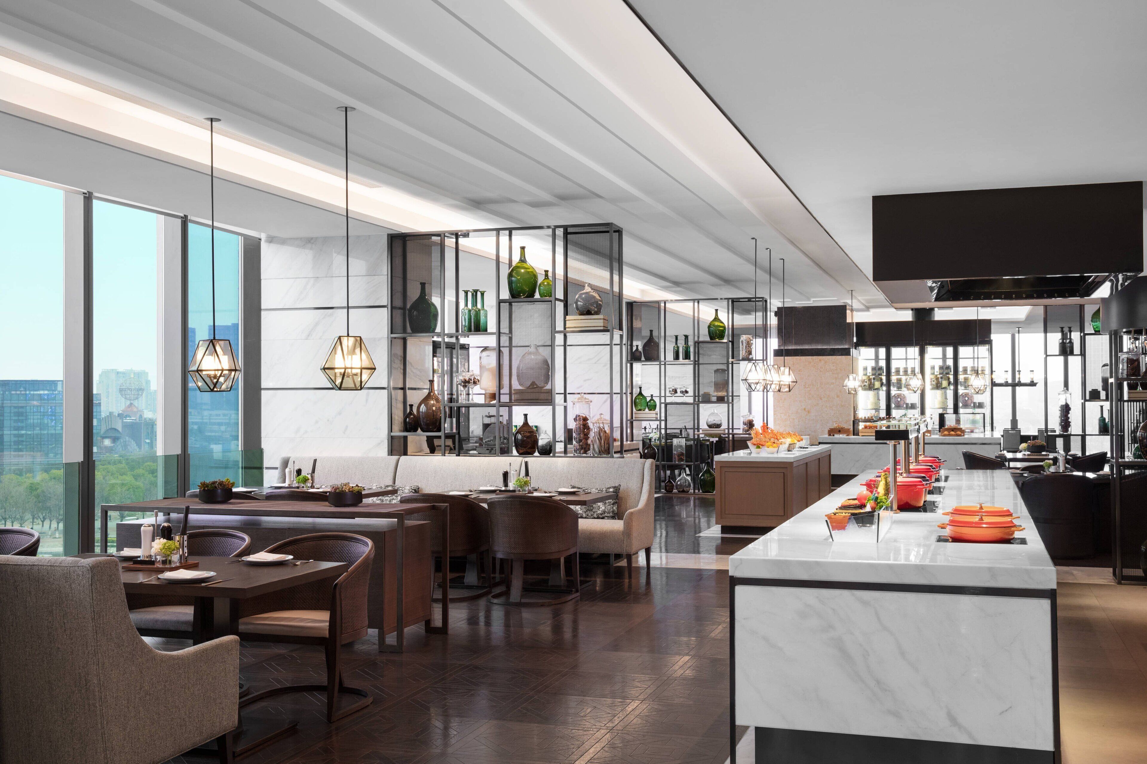 A modern kitchen with a marble island, dining area with chairs, and a view of the city through large windows.