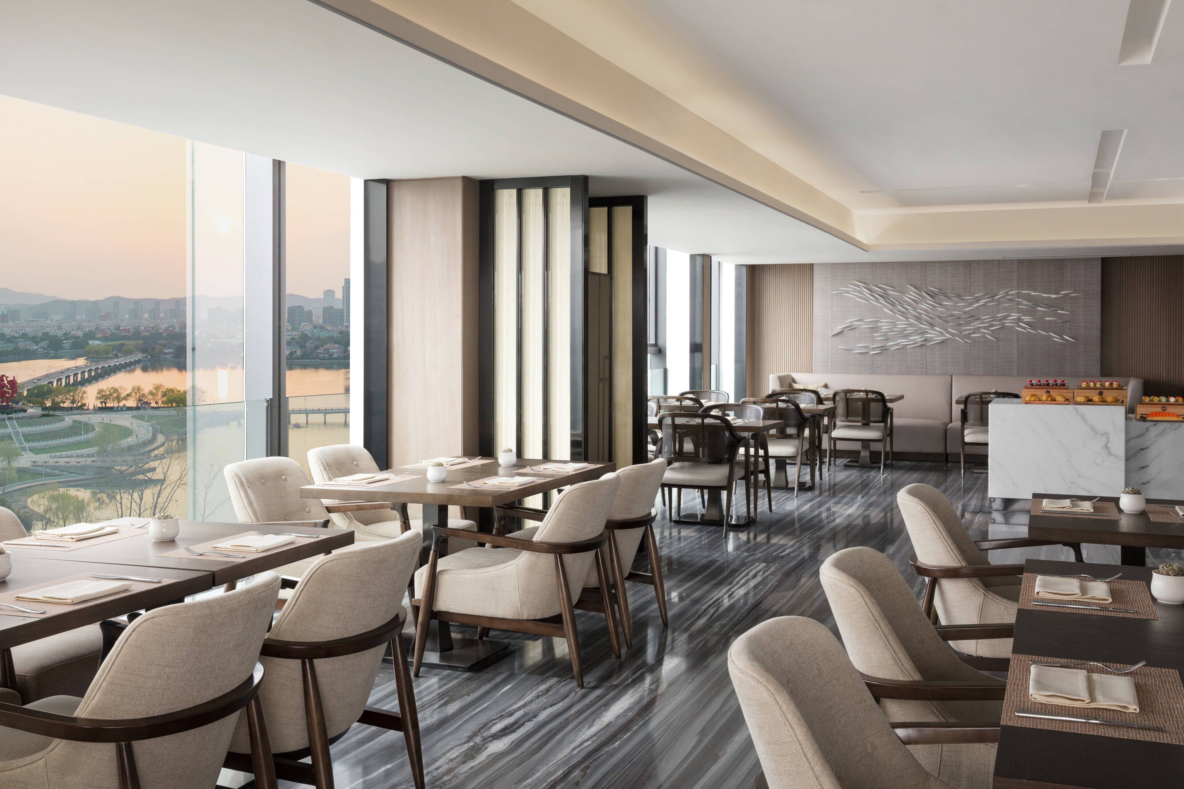 A modern dining area with high tables and chairs, large windows offering a view of a cityscape and river.