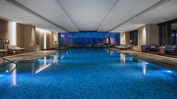 Une piscine intérieure moderne avec vue sur la ville, des espaces de détente et une configuration spacieuse.