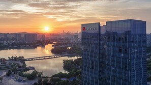 Ein modernes Hochhaus mit sichtbarem Marriott-Logo, umgeben von einer Stadtansicht und einem Fluss mit einer Brücke.
