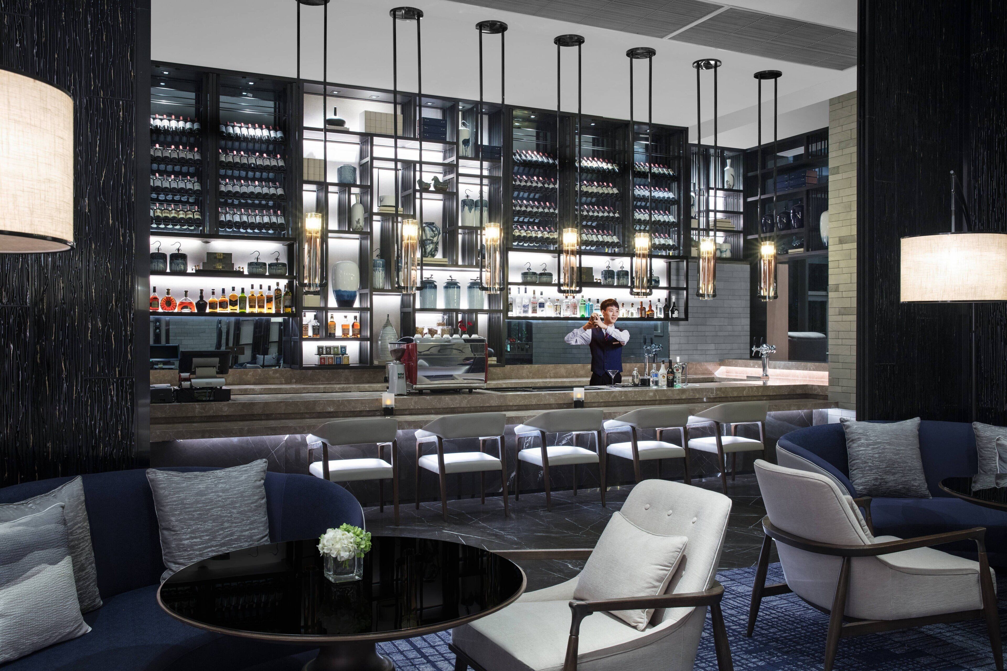 Zona de bar moderna con exhibición de vinos y licores, diferentes disposiciones de asientos y una barra.