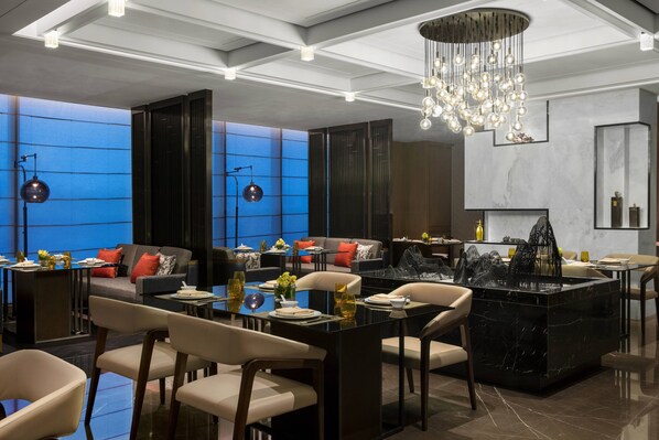 A modern hotel lobby with a central seating area, a black marble fountain, and a chandelier.