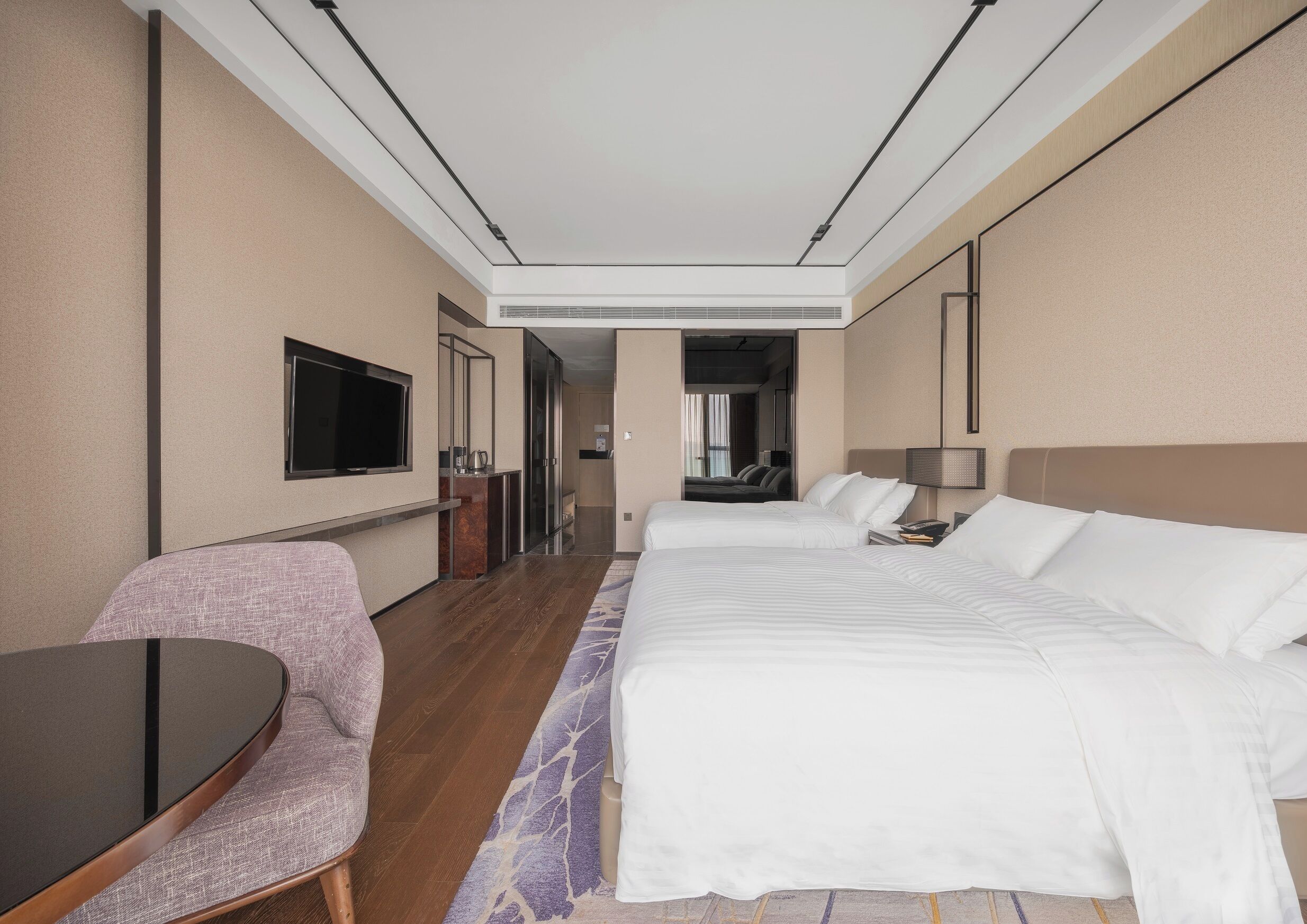 A hotel room with a large bed, a desk, a chair, a TV, and a bathroom visible through an open door.