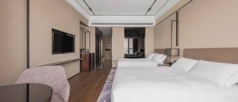 A hotel room with a large bed, a desk, a chair, a TV, and a bathroom visible through an open door.