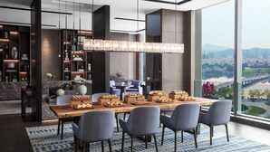 Un espace repas moderne, doté d’une grande table, de chaises et offrant une vue sur la ville grâce à de larges fenêtres.
