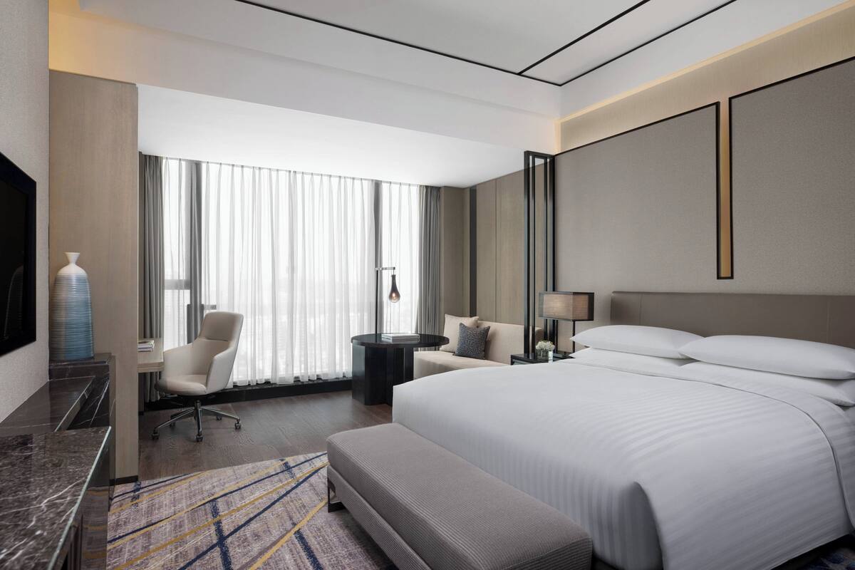 Ein modernes Hotelzimmer mit einem großen Bett, einem Schreibtisch, einem Sessel, einem kleinen Tisch und einem Fernseher.