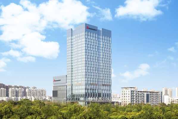 Ein modernes Hochhaus-Hotel mit Glasfassade, umgeben von anderen Gebäuden und Grünflächen.