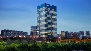 Un hôtel Marriott moderne, à la façade structurée en forme de grille, entouré d’autres bâtiments et d’arbres.