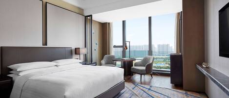 Habitación de hotel moderna con una cama grande, un escritorio con silla, un televisor y vistas a la ciudad.