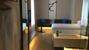 A modern hotel room with a large bed, a bedside table, a mirror, and a seating area with a sofa and a small table. - Fairfield by Marriott Shanghai Jingan (Shanghai)