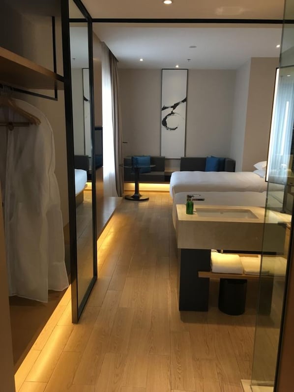 A modern hotel room with a large bed, a bedside table, a mirror, and a seating area with a sofa and a small table.