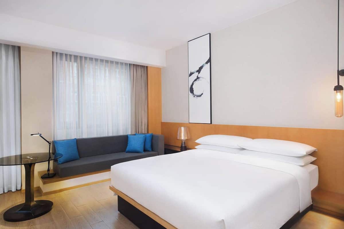 A hotel room with a large bed, a sofa, a small table, and a lamp.
