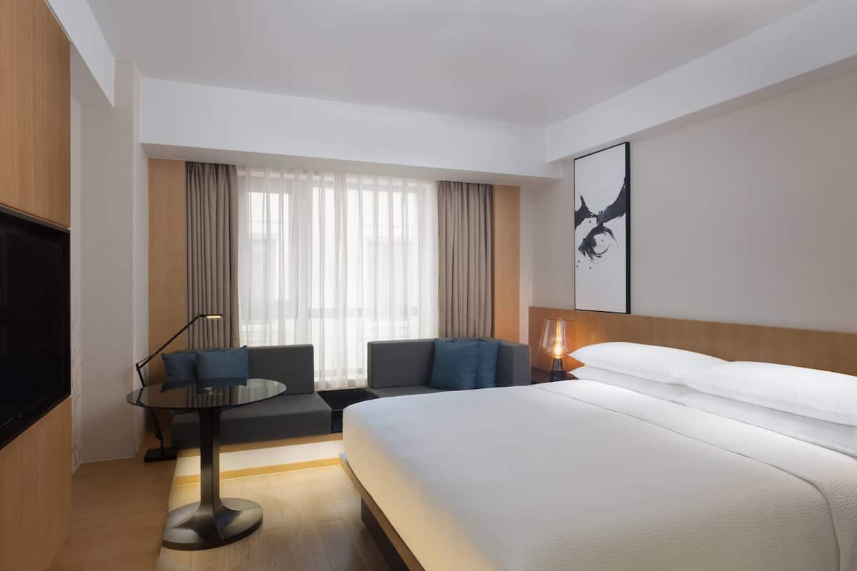 A modern hotel room with a large bed, a sofa, a small table, and a TV.