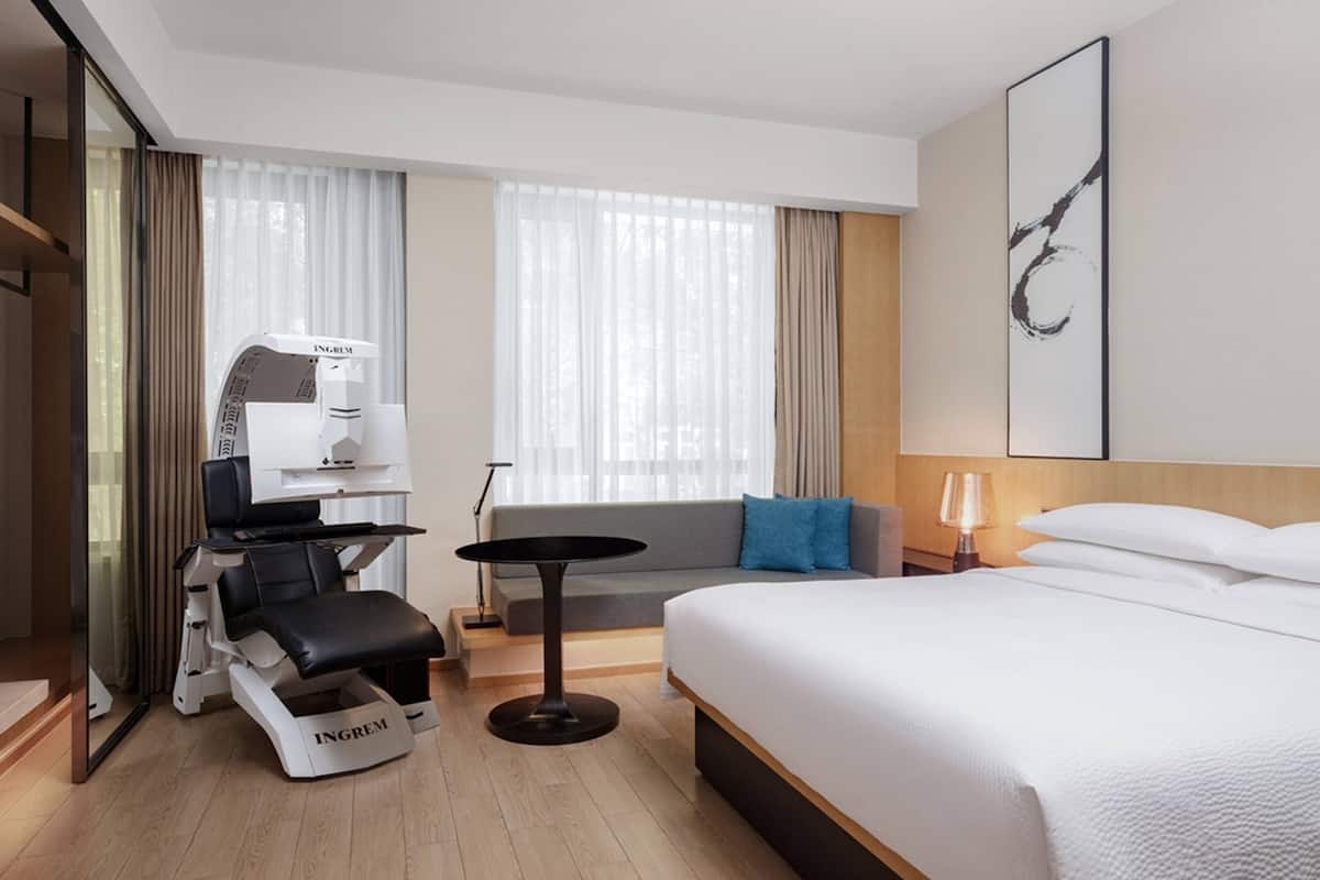 A modern hotel room with a bed, a seating area with a table, a massage chair, and a massage machine.