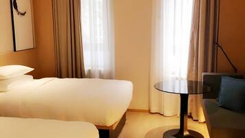 Quarto de hotel com duas camas, uma mesa redonda e um sofá.