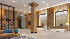 A modern lobby with a reception desk, a bookshelf, a sofa, and a large pillar. - Fairfield by Marriott Shanghai Jingan (Shanghai)