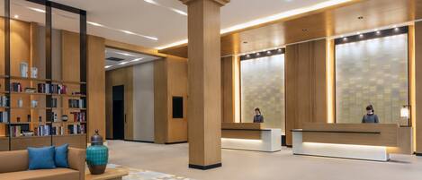 A modern lobby with a reception desk, a bookshelf, a sofa, and a large pillar.
